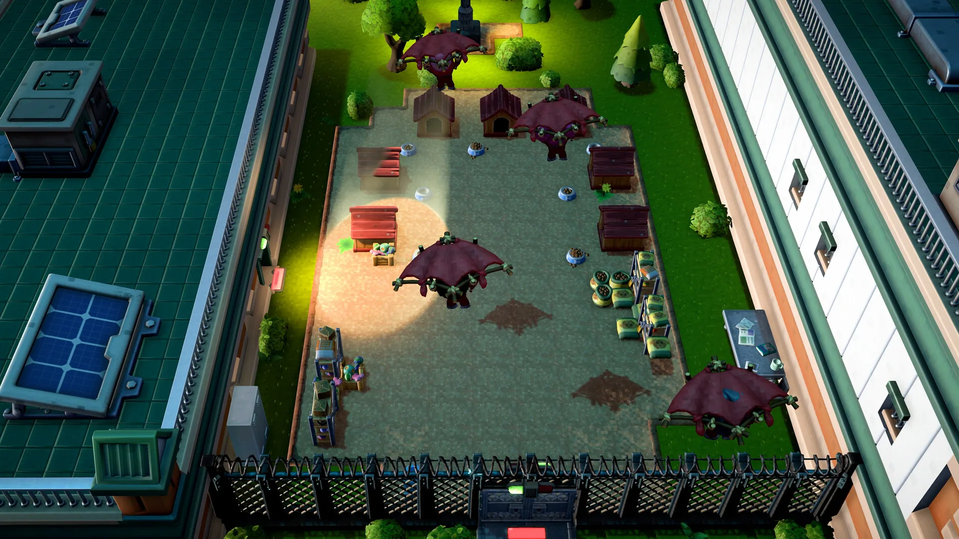 Official The Escapists 3 screenshot showing a fenced dog kennel yard between two prison buildings at night with a bright spotlight sweeping the ground